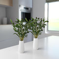 Detailaufnahme eines künstlichen Olivenzweigs mit grünen Blättern in Keramikvase