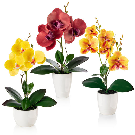 Drei künstliche Orchideen in bunten Farben in weißen Keramiktöpfen