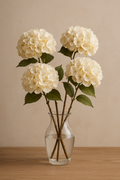Vier cremefarbene künstliche Hortensien in einer Glasvase auf einem Holztisch vor einer beigen Wand – elegante Kunstblumen-Deko für Wohnzimmer, Hochzeit oder Tischgestaltung.